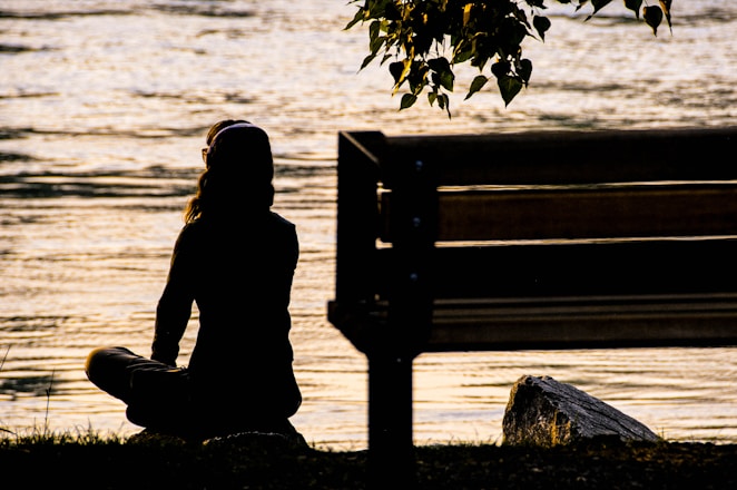 silhouette of person sitting on bench near body of water during daytime