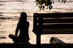 silhouette of person sitting on bench near body of water during daytime