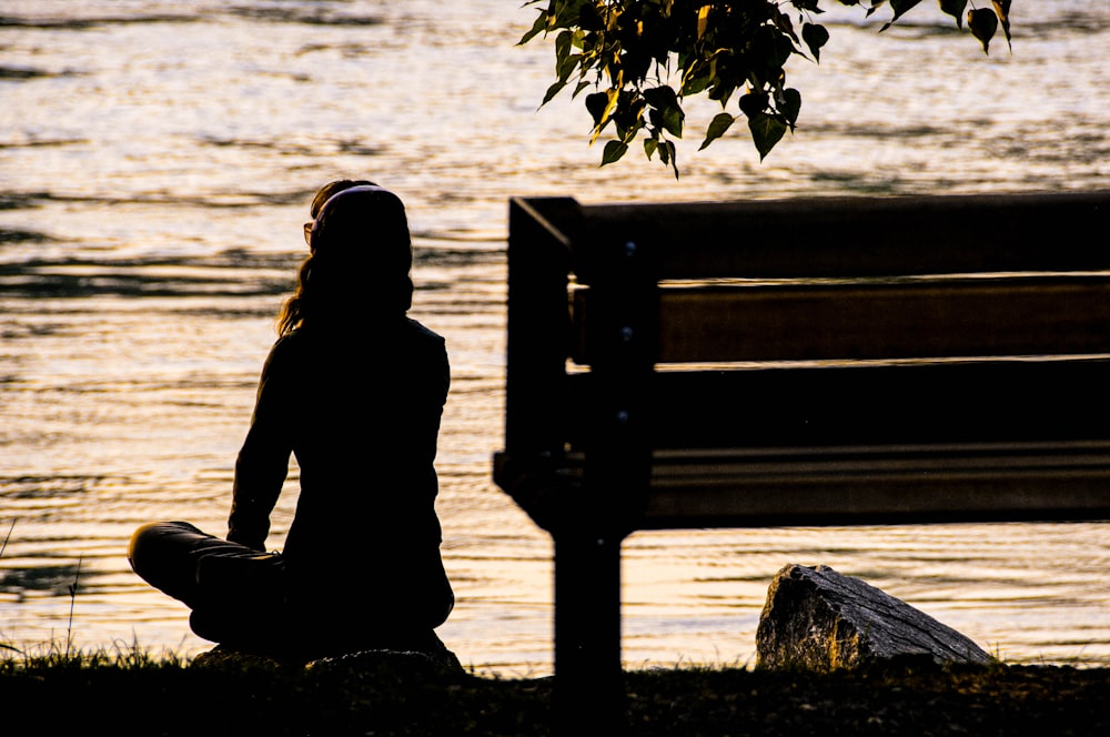 Silhouette der Person, die tagsüber auf einer Bank in der Nähe des Gewässers sitzt