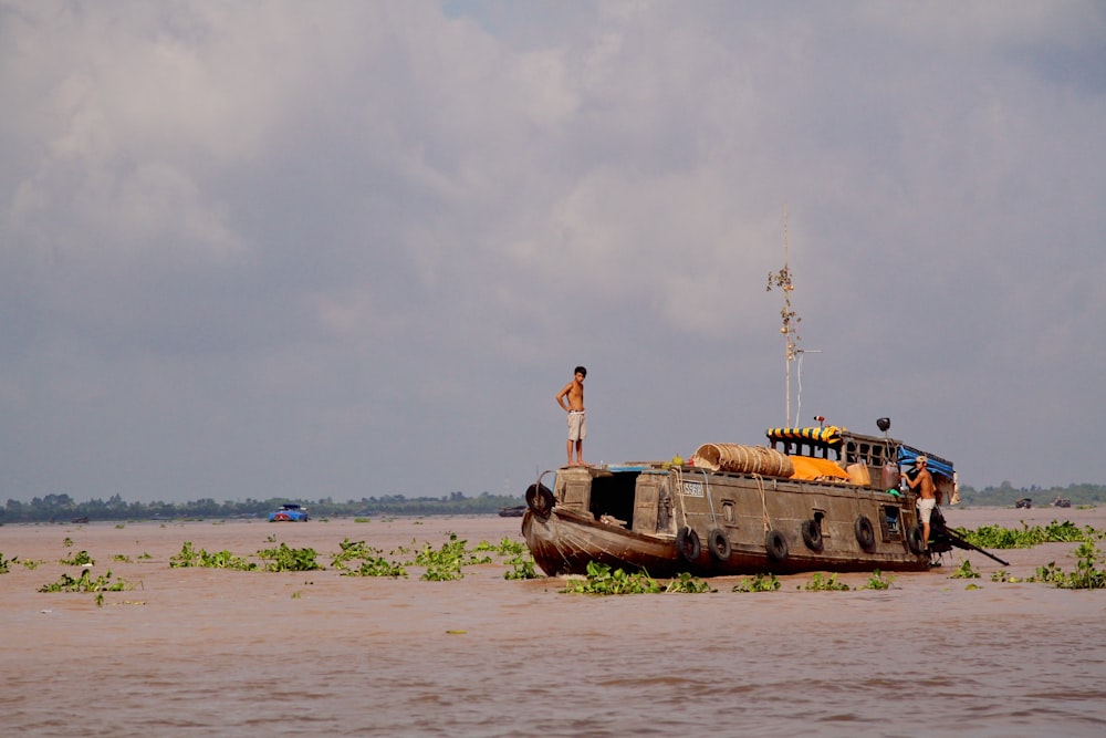 man in white t-shirt and black shorts standing on brown wooden boat on sea shore