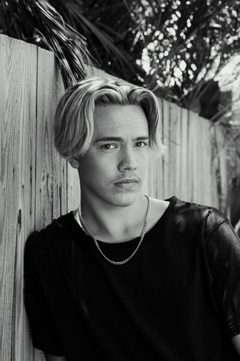 a black and white photo of a man leaning against a fence