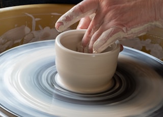 person making clay pot on white round plate