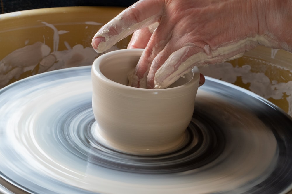 personne faisant un pot en argile sur une assiette ronde blanche