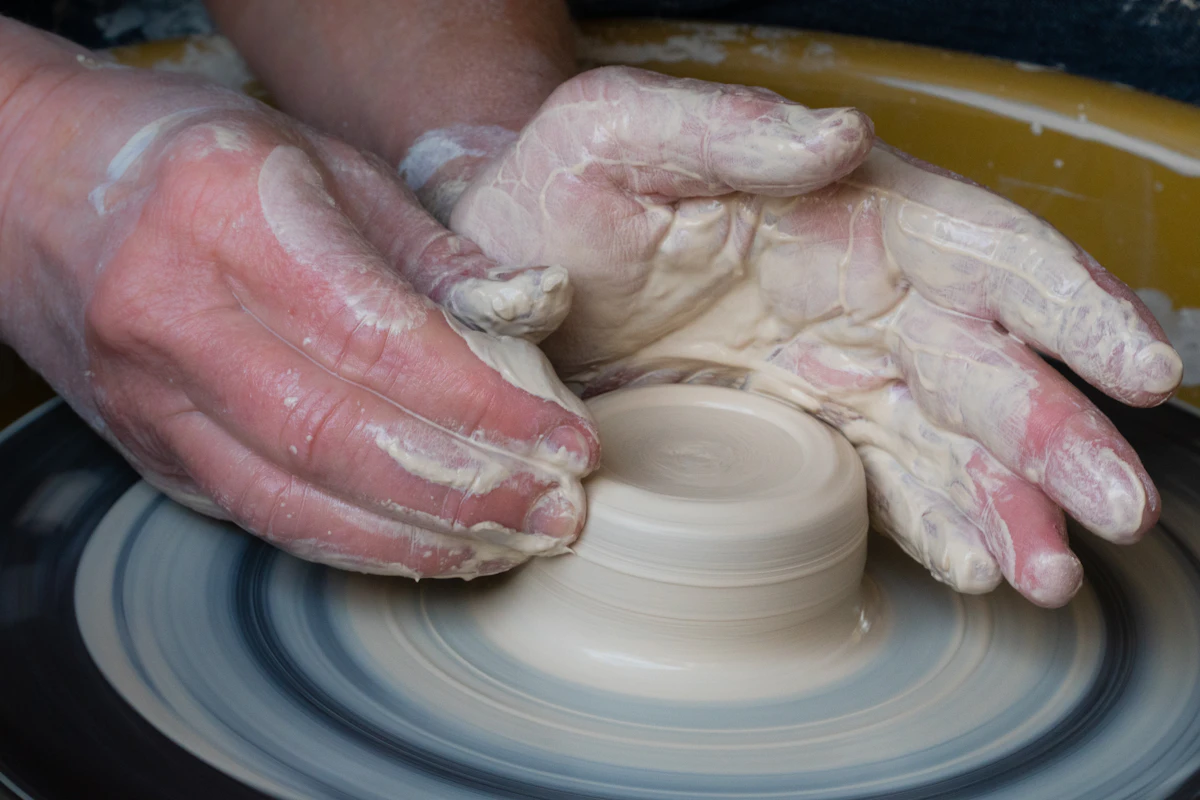 Clay-covered hands shaping a bowl on a spinning potter's wheel