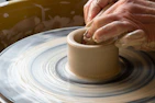 A close-up of a potter’s hands shaping a clay heart on the wheel, surrounded by bright glazes.