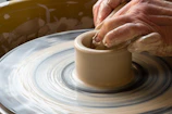 Close-up of a hand shaping clay on a potter’s wheel, with splashes of bright glaze nearby.