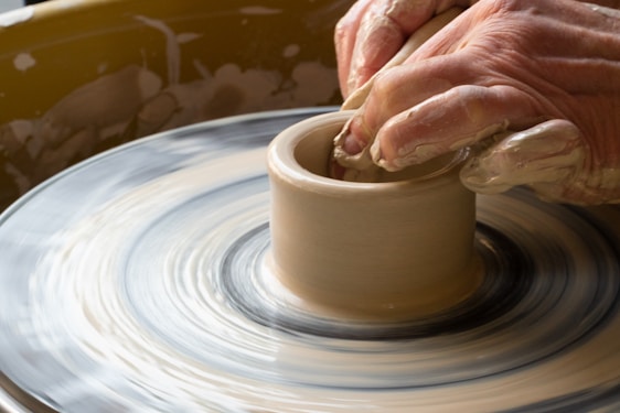 A close-up of hands gently molding a clay pot on a spinning wheel, with soft natural light highlighting the texture.