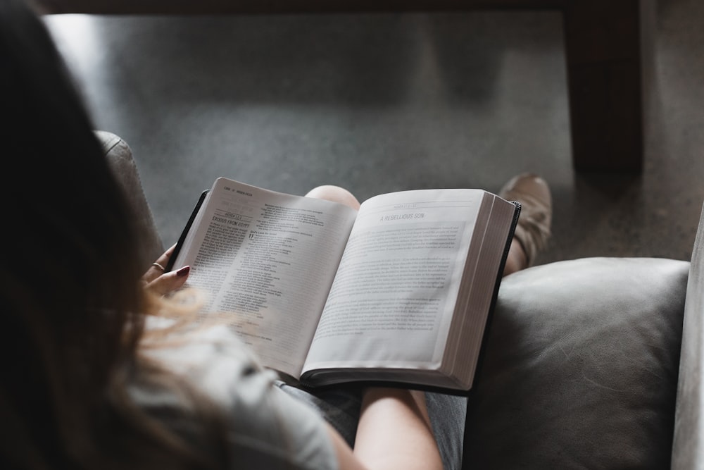 person reading book on black leather couch