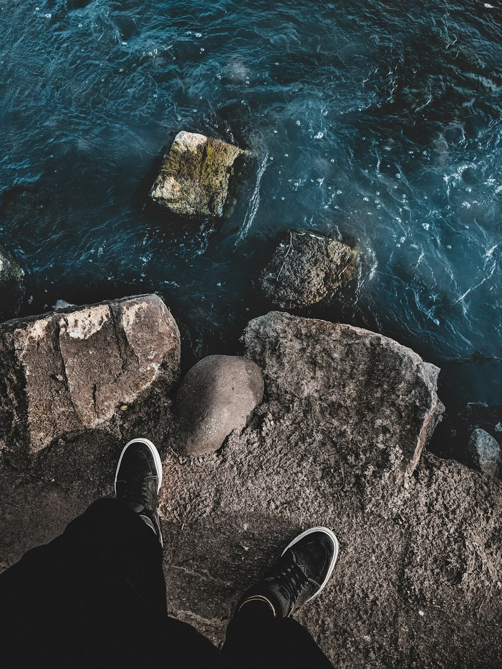 person in black pants and black shoes standing on rocky shore