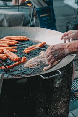 Artisan hands shaping and frying crunchy snacks in a large pan over an open flame.