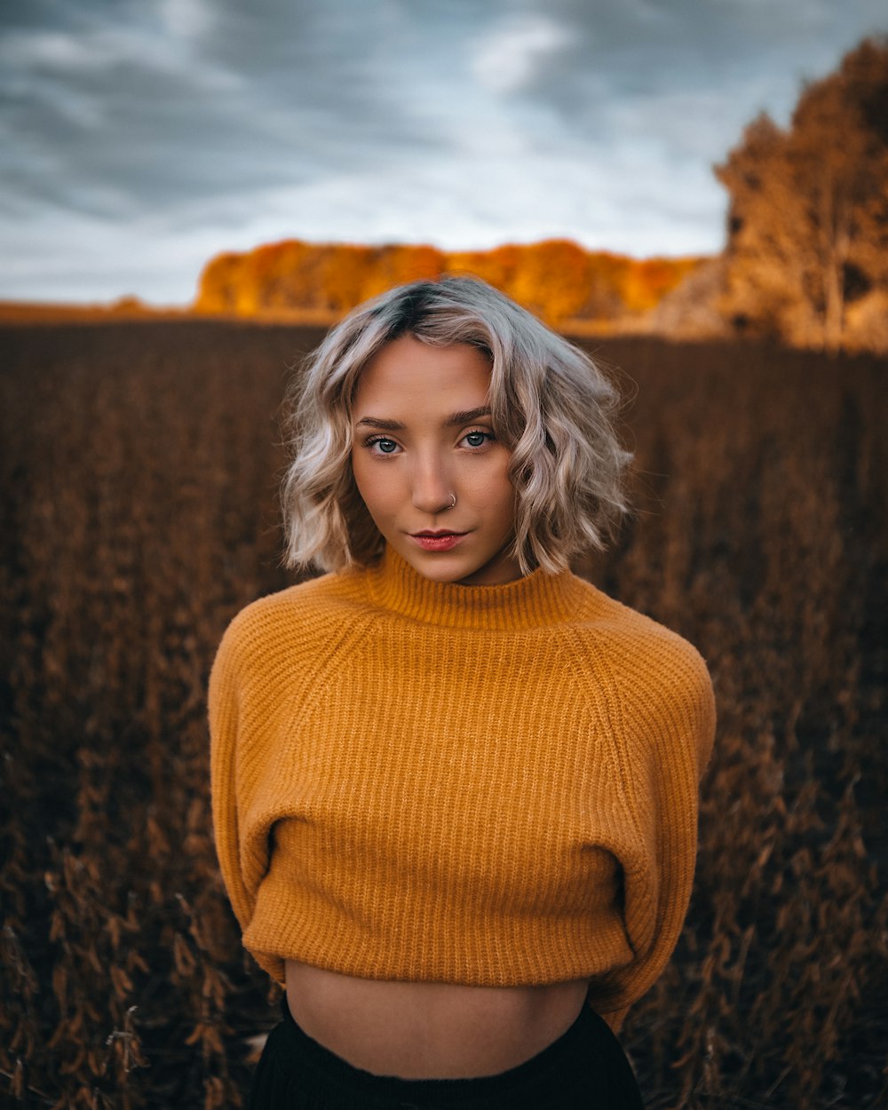 donna in maglione dolcevita marrone in piedi sul campo di erba marrone durante il giorno