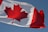 A large red maple leaf is centered on a white square background, with red vertical bars on either side. The flag is slightly rippling in the wind against a clear blue sky.