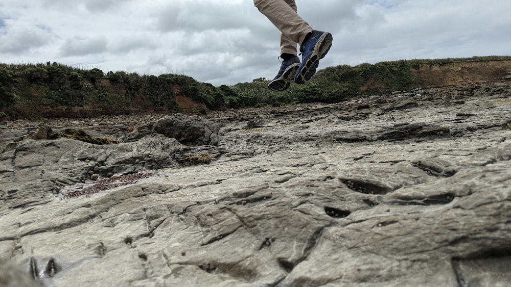 person in gray pants and black and white sneakers standing on rocky mountain during daytime