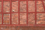 Brick wall with a rustic appearance featuring red wooden beams intersecting the brickwork in a traditional pattern. The bricks vary slightly in color, adding texture and depth.
