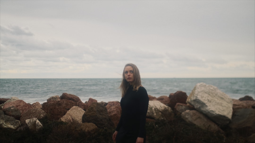 woman in black long sleeve shirt standing on brown rock near body of water during daytime