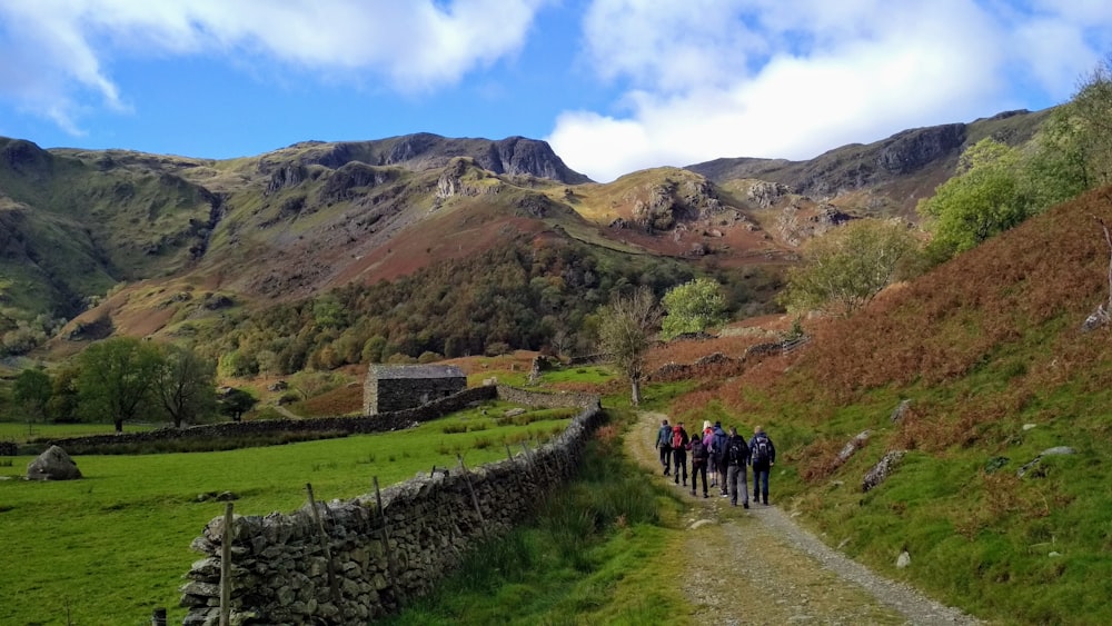 people walking on green grass field near mountain under blue sky during daytime