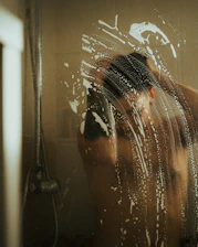 Close-up of hands applying shampoo to wet hair in a bright bathroom.
