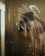 A person is seen through a glass shower door covered with soap suds. The individual is washing their hair, and the details are slightly obscured by the opaque soap patterns on the glass. The image has dim lighting, providing a private and intimate atmosphere.