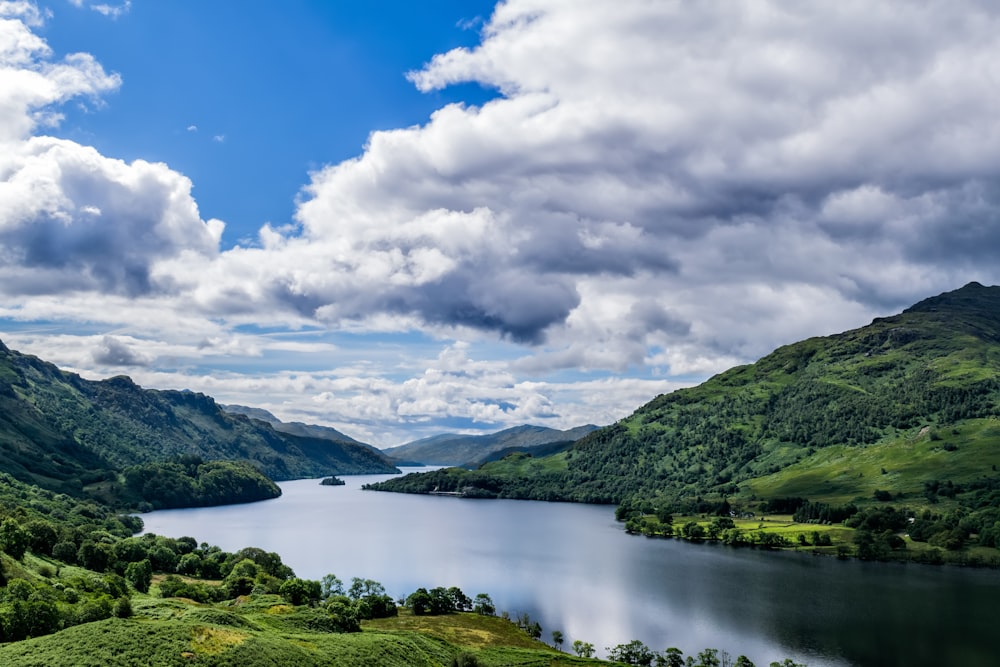 green mountains beside lake under blue sky and white clouds during daytime