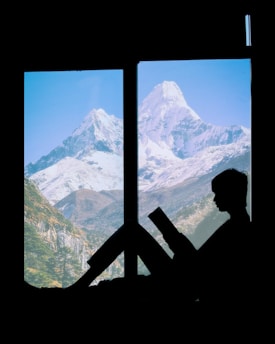 Cozy person reading an e-book on a tablet by a window with a scenic mountain view in the background.