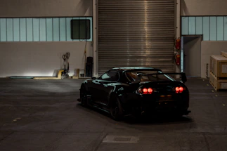 A sleek black sports car illuminated by red garage lights, spotlighting its polished details.