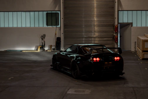 A sleek black sports car illuminated by red garage lights, spotlighting its polished details.