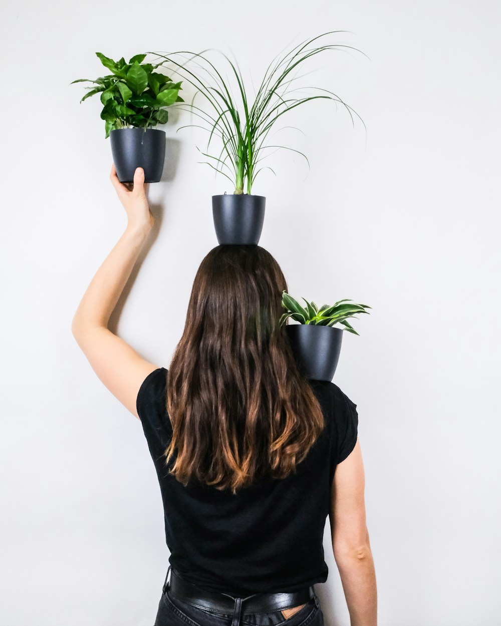 緑の鉢植えの植物を持つ黒いノースリーブのシャツを着た女性