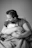 A serene mother holding her sleepy baby in a cream linen armchair by a softly lit window.