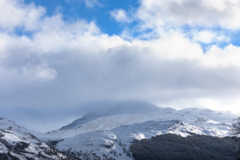 montañas cubiertas de nieve bajo nubes blancas y cielo azul durante el día