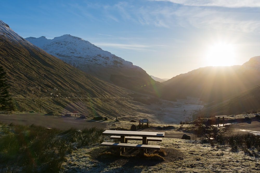 Tavolo da picnic in legno marrone sul campo di erba verde vicino alle montagne durante il giorno