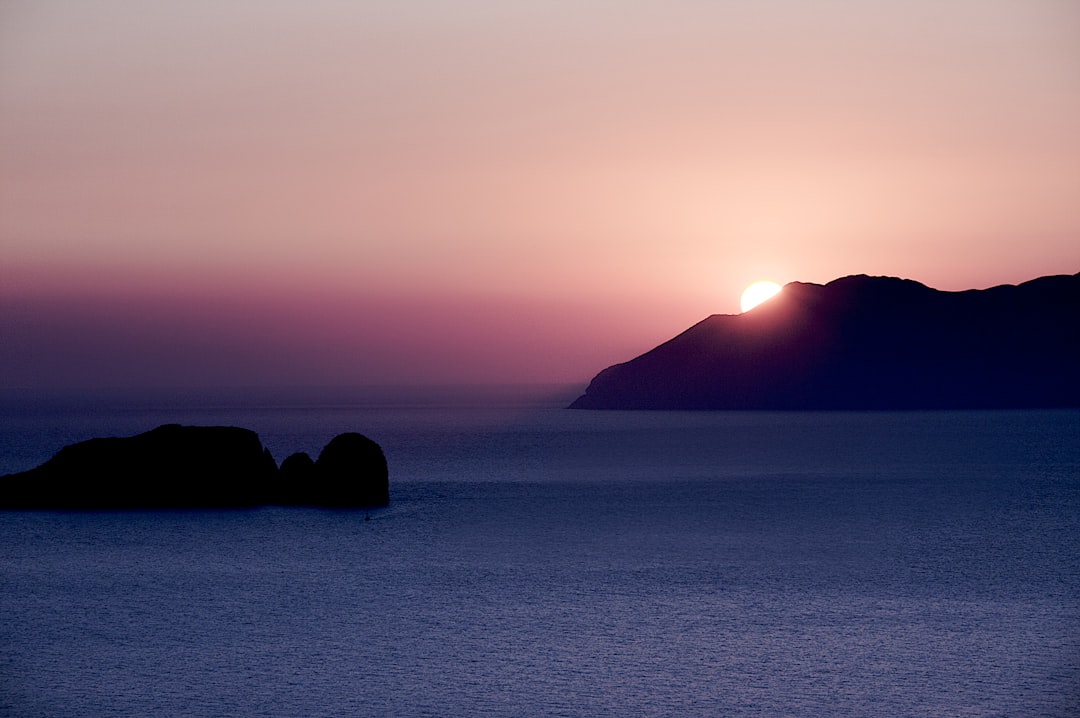 silhouette of mountain beside body of water during sunset