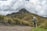 man in gray jacket and black pants walking on dirt road near green grass field during