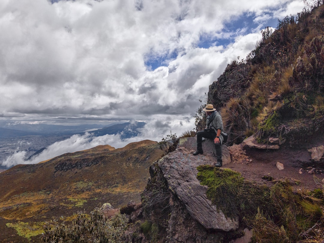 man in black jacket and black pants standing on rock formation under white clouds and blue,