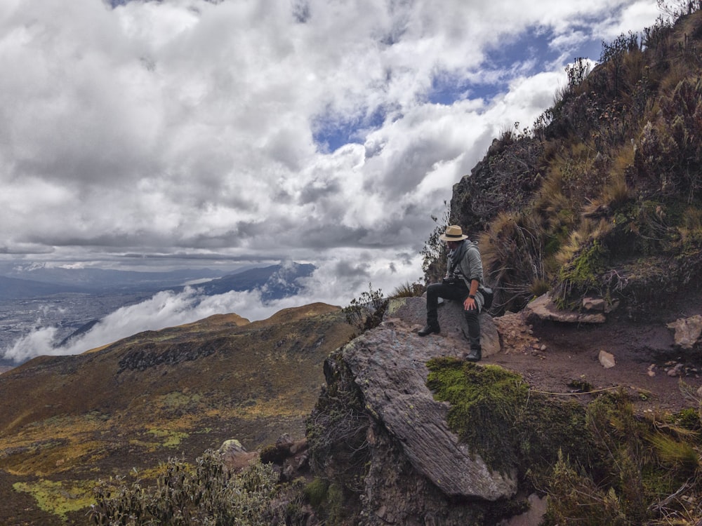 man in black jacket and black pants standing on rock formation under white clouds and blue