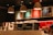 Warmly lit coffee shop interior with a modern espresso machine, stacks of takeaway cups, and colorful menu boards on the wall. Three pendant lamps hang above the counter, creating a cozy atmosphere.