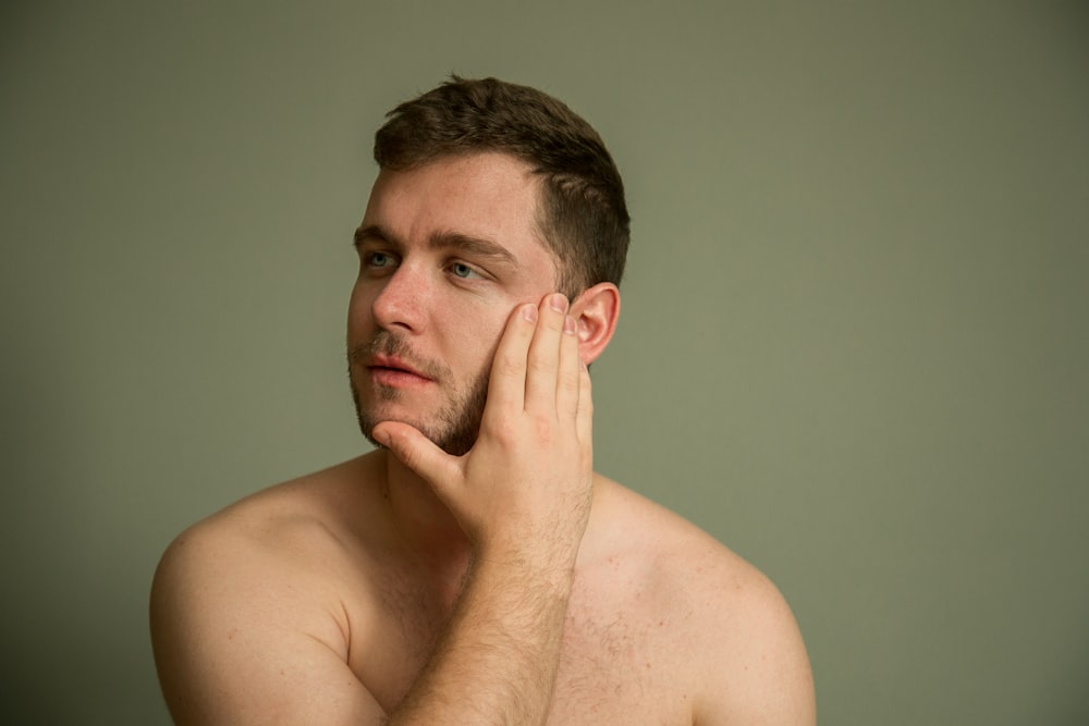 topless man covering his face with his hand