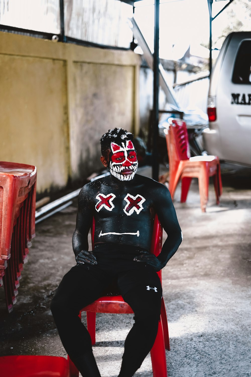 man in black and white mask sitting on red plastic chair