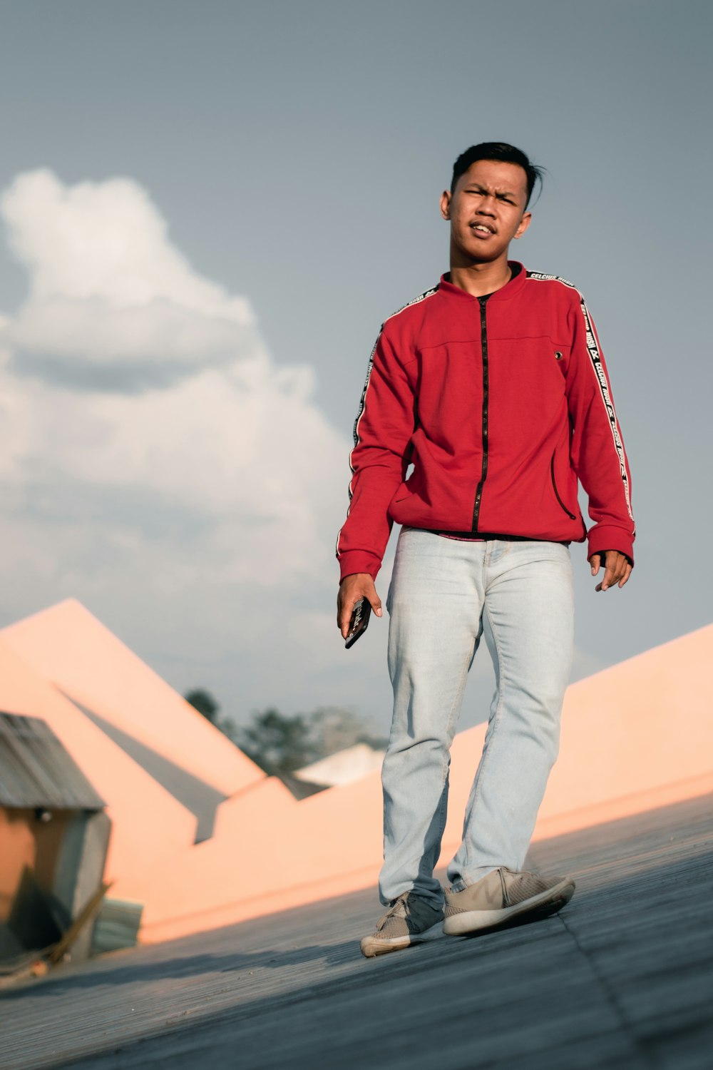 man in red dress shirt and blue denim jeans standing on white concrete wall during daytime