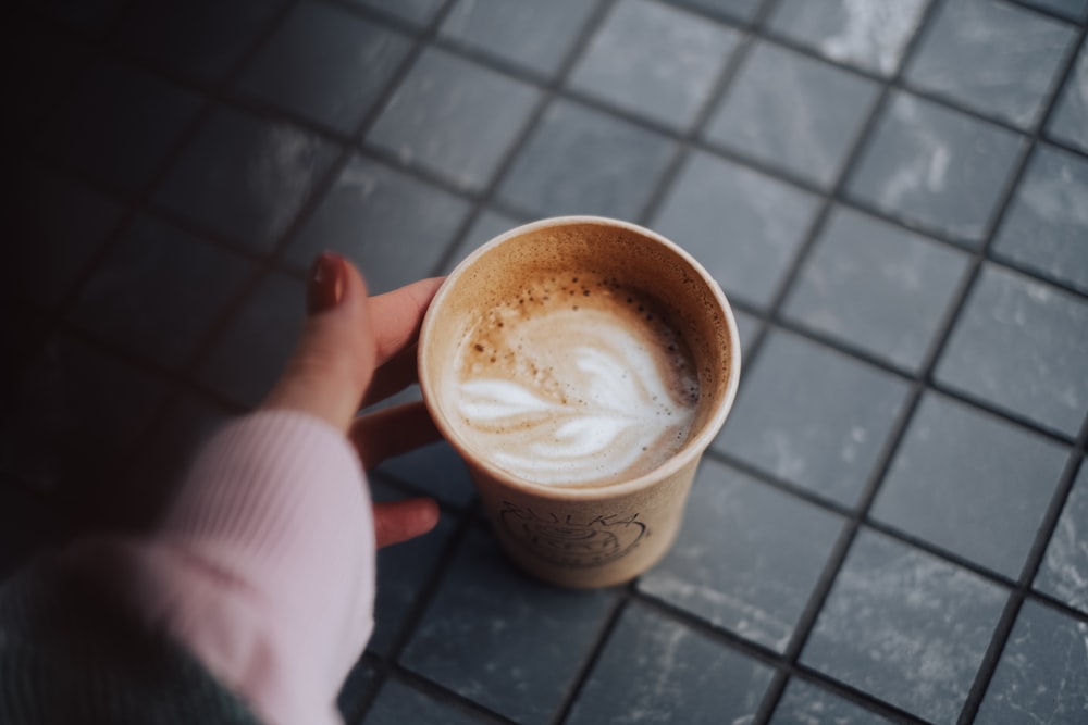 a person holding a cup of coffee on a tiled floor