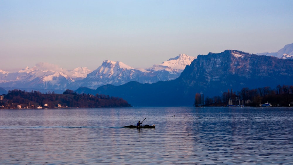 person riding on boat on lake near mountain range during daytime