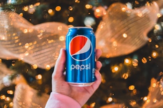 Close-up of hands holding colorful Carnavalera foam cans with festive decorations in the background.