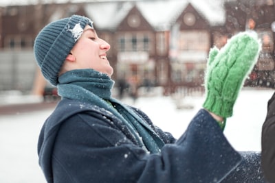 woman in black coat and green knit scarf mittens teams background
