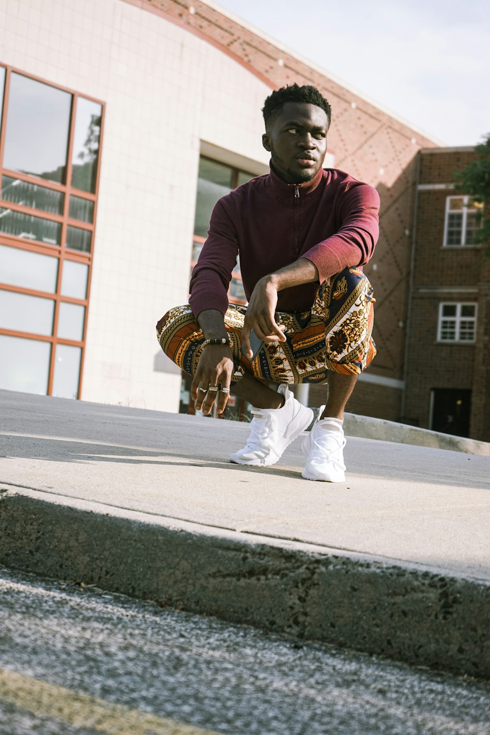 man in purple long sleeve shirt and white pants sitting on gray concrete floor