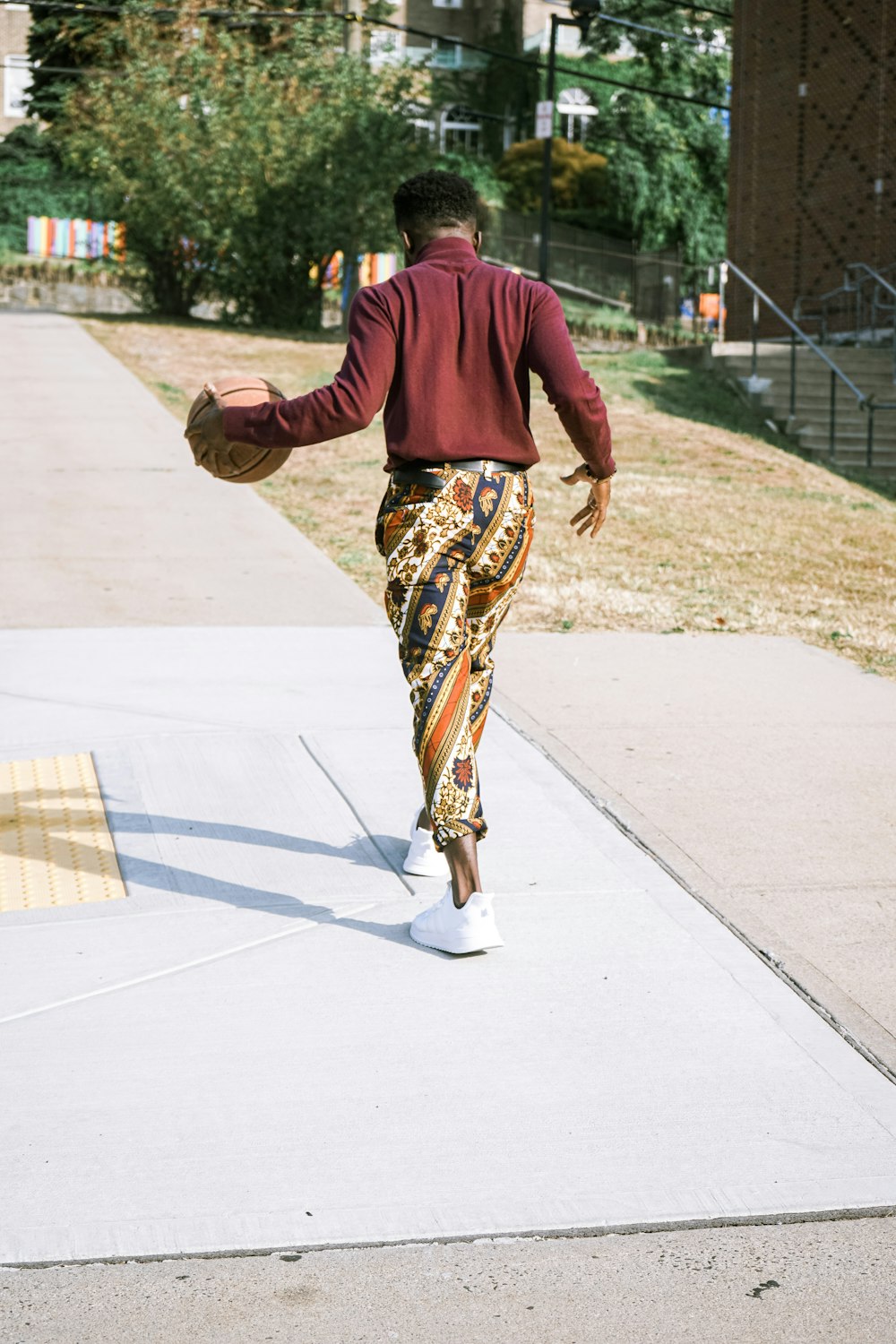 man in red long sleeve shirt and brown pants walking on gray concrete pavement during daytime