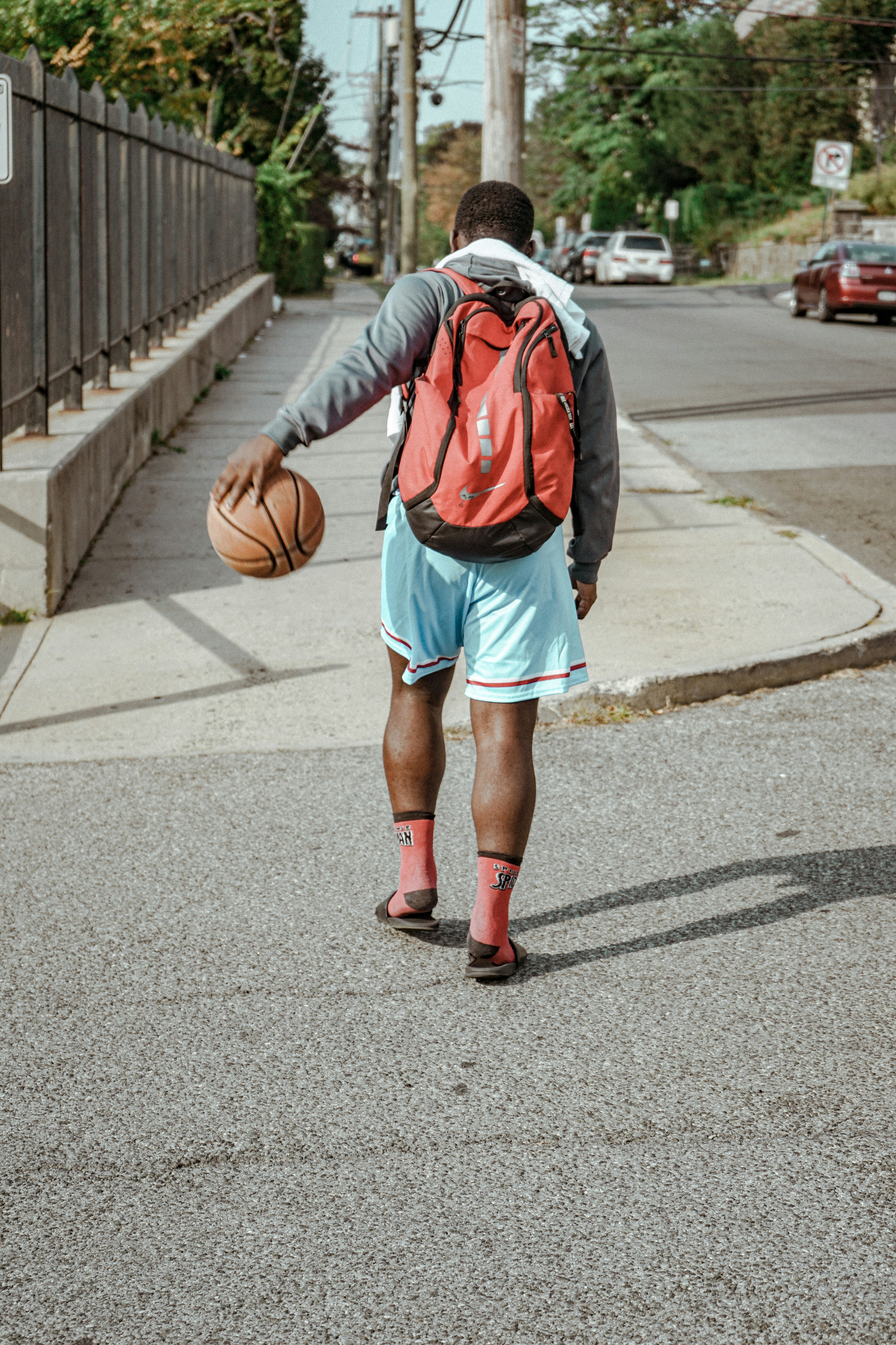 man in red and gray hoodie and blue shorts walking on gray asphalt road during daytime