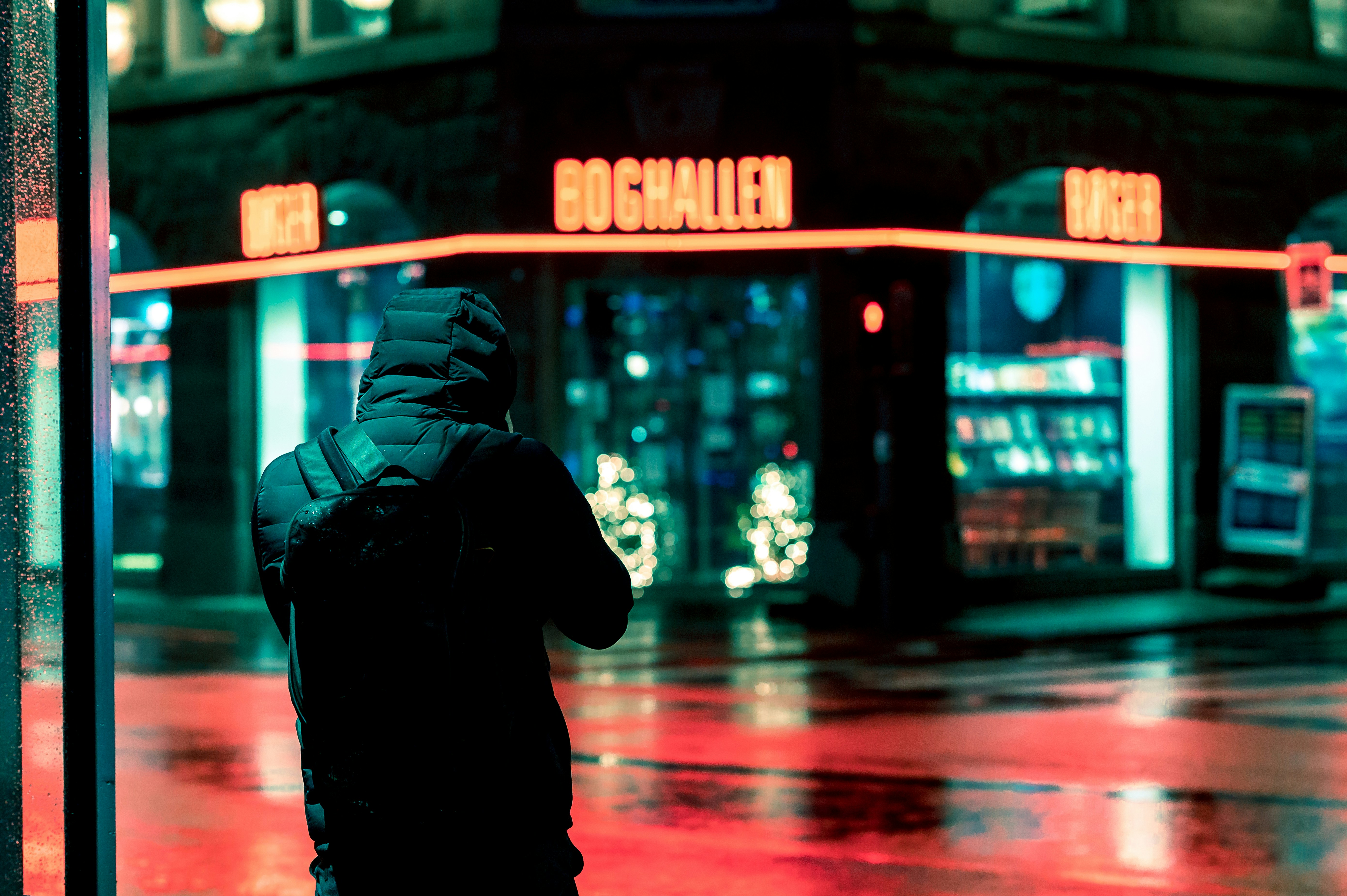 homem em capuz preto em pé na calçada durante a noite