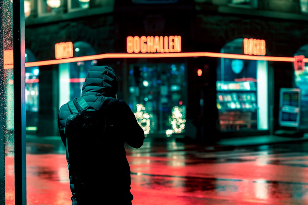 man in black hoodie standing on sidewalk during night time