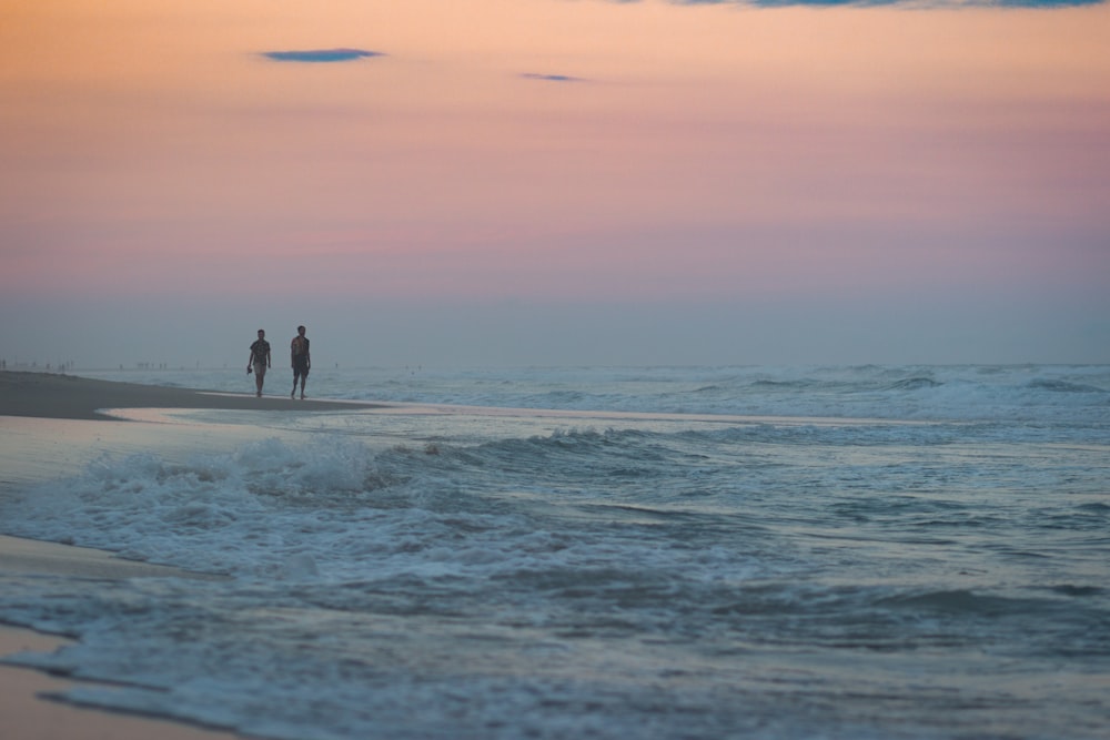 2 people walking on beach during sunset