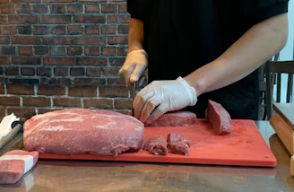 Butcher carefully trimming fresh lamb meat wearing hygiene gloves.