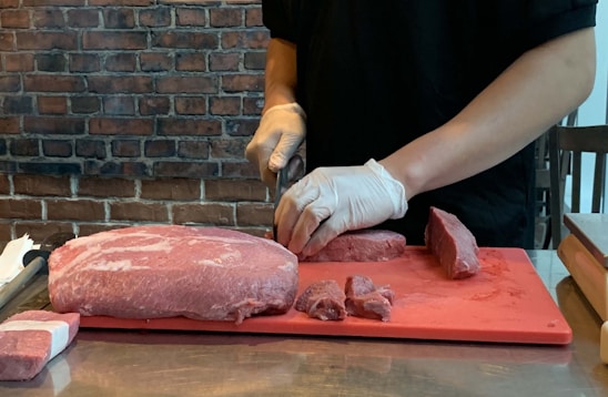 A professional meat packer wearing gloves carefully packaging fresh cuts of meat in a clean facility.